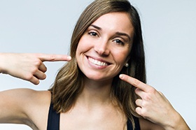 Woman pointing at her smile after undergoing cosmetic dental treatment