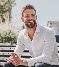Man in white shirt sitting on a bench and smiling 