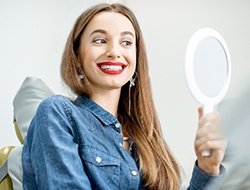 Woman with mirror enjoying aesthetic benefits of dental crowns