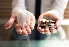 Hand holding coins and model tooth representing cost of dental implants in Marshall