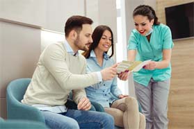 Dentist and couple reviewing the cost of implant dentures in Marshall 