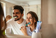 Young couple brushing teeth to prevent dental emergency in Marshall