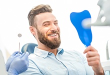 Man using mirror to admire his implant-supported teeth