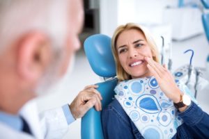 a woman touching her mouth in pain at the dentist office