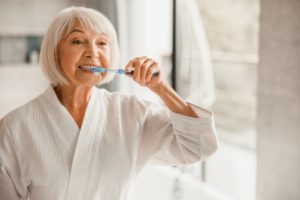 senior woman brushing teeth to protect oral health during quarantine