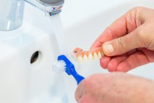 Caring for dentures by cleaning them with soft-bristled brush