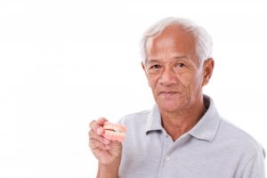 Senior man holding full dentures, wondering about using denture adhesive