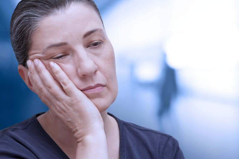 Older woman holding her cheek due to denture sores